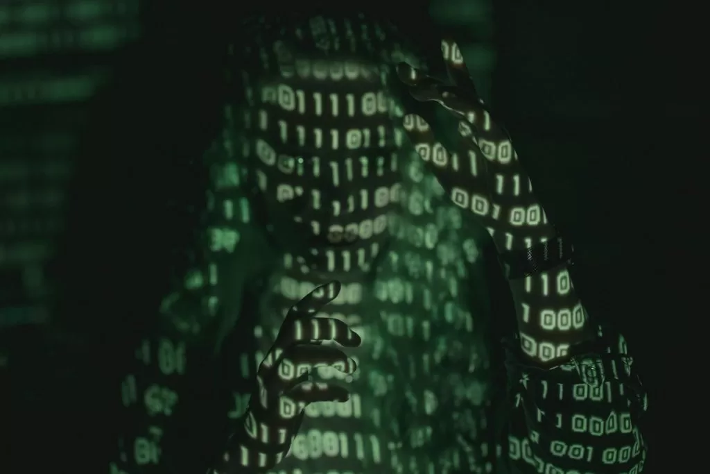 Image shows the silhouette of a person with a projection of computer codes on his face;  the image is greenish on a dark background